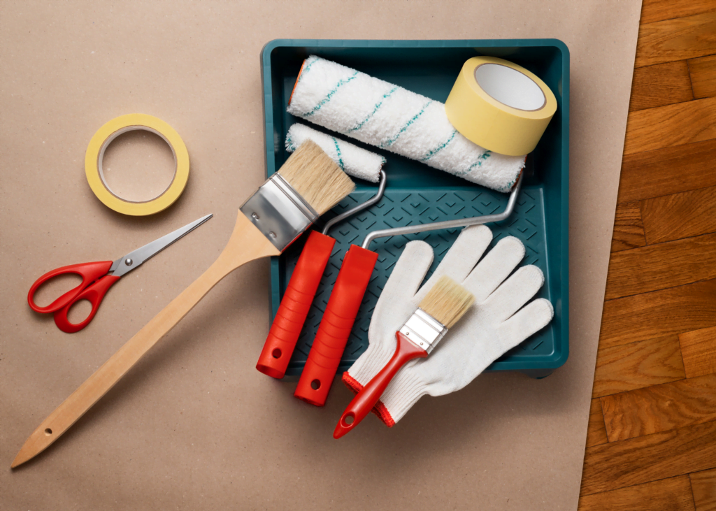 Essentials for a Flawless Paint Job - Ocala Handyman Co. Website - Ocala Handyman Co. Website Close-up of house painting supplies including scissors, gloves, tapes, paint brushes, and rollers