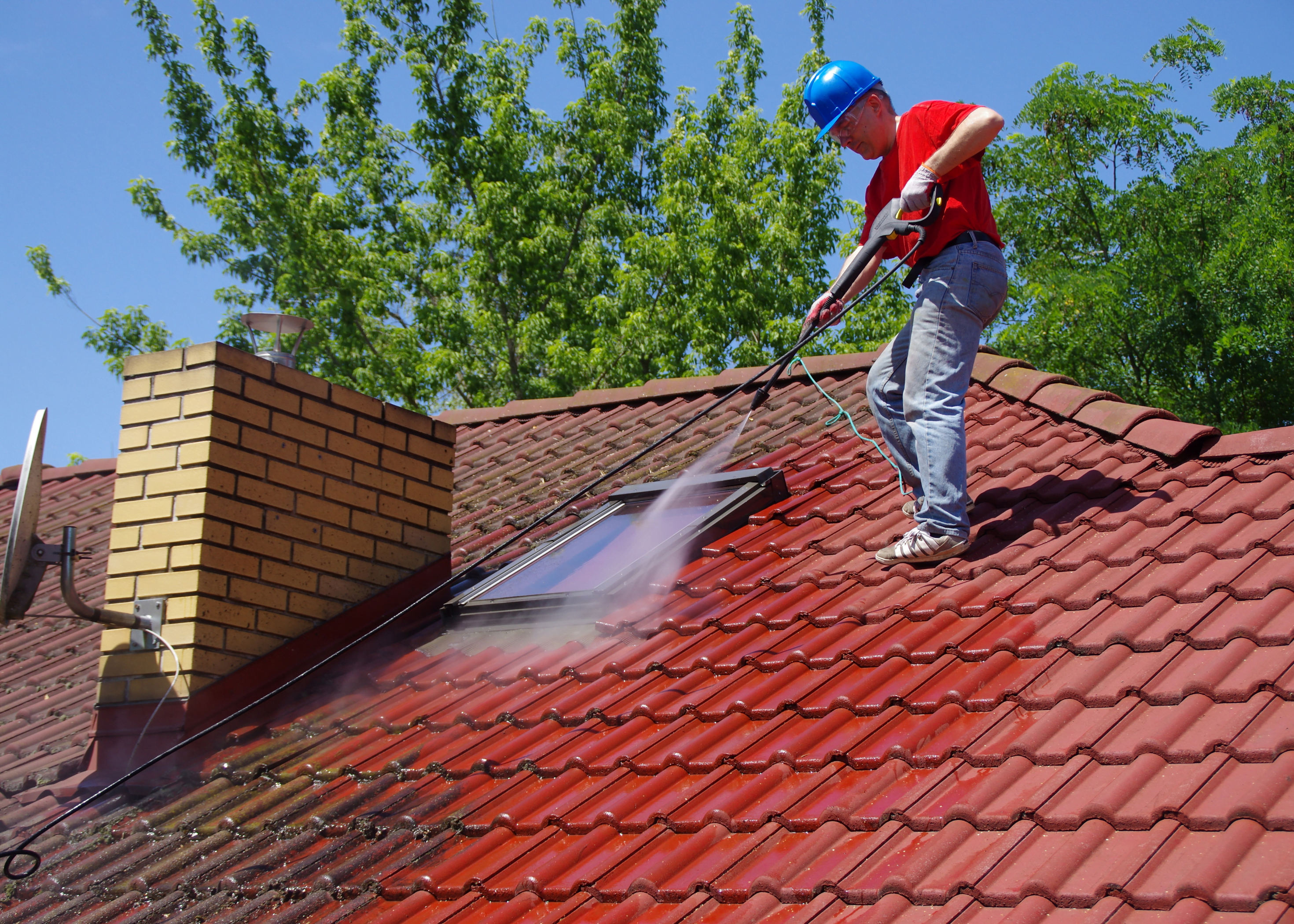Worker on top of a house roof, cleaning tiles with a professional pressure tool, part of Ocala Handyman Co.'s Cleaning Services in Ocala, FL